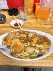 広宣的廣式炒麵與桌旁飲料，麵上鋪著蔬菜及肉片